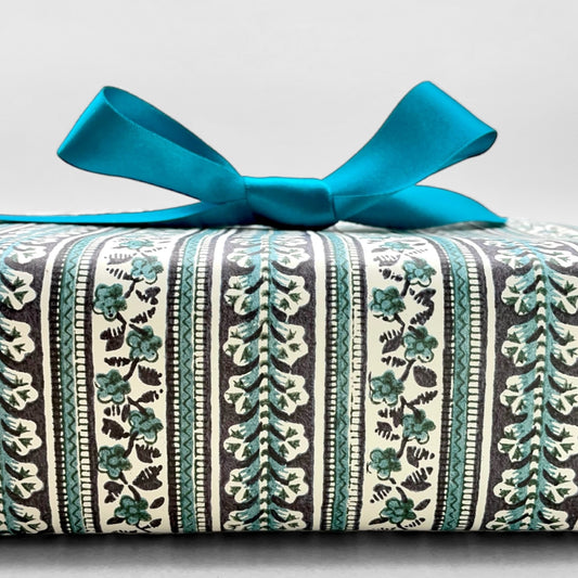 italian Remondini patterned wrapping paper by Tassotti. Striped design with bands of flowers in dark navy and teal on cream backdrop. Shown as a wrapped present with teal ribbon bow.