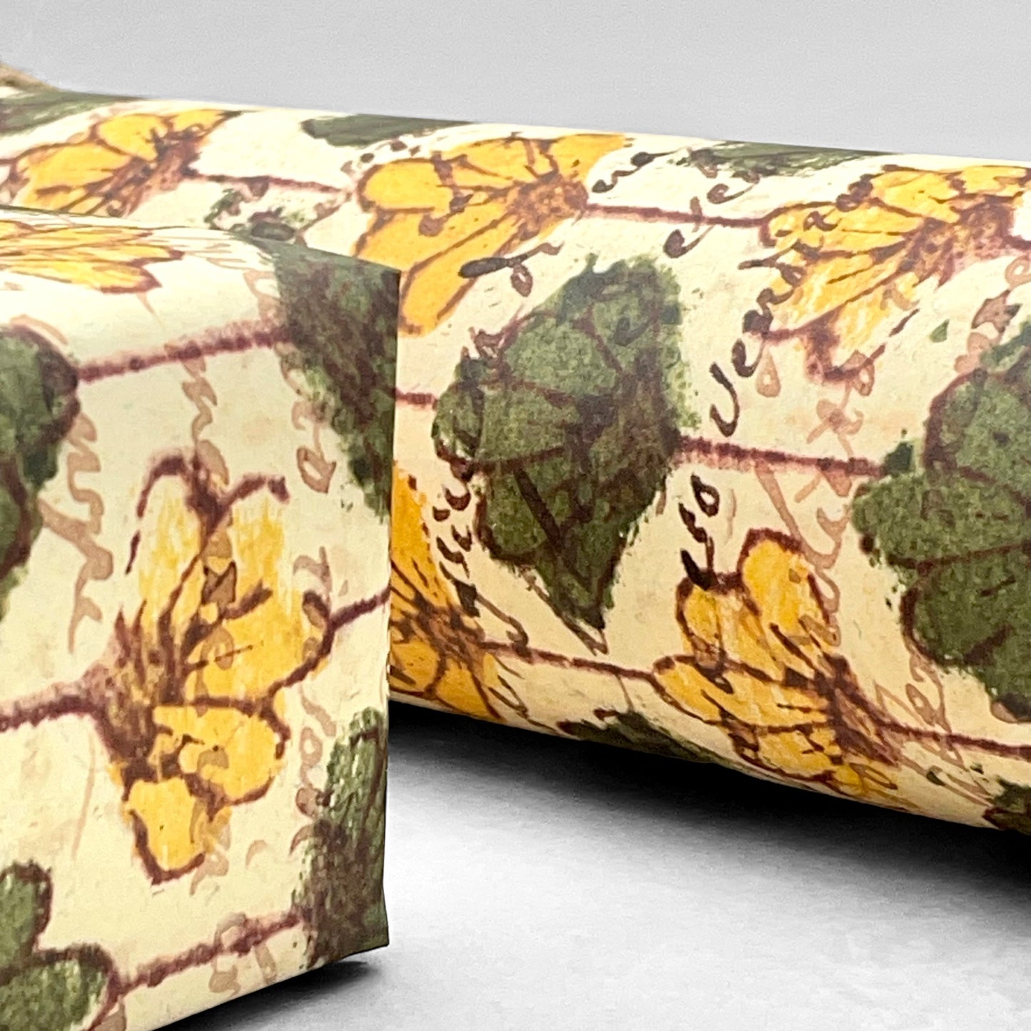 italian Remondini patterned wrapping paper by Tassotti. Repeat floral pattern with yellow and green flowers on a beige background with script writing. Close up