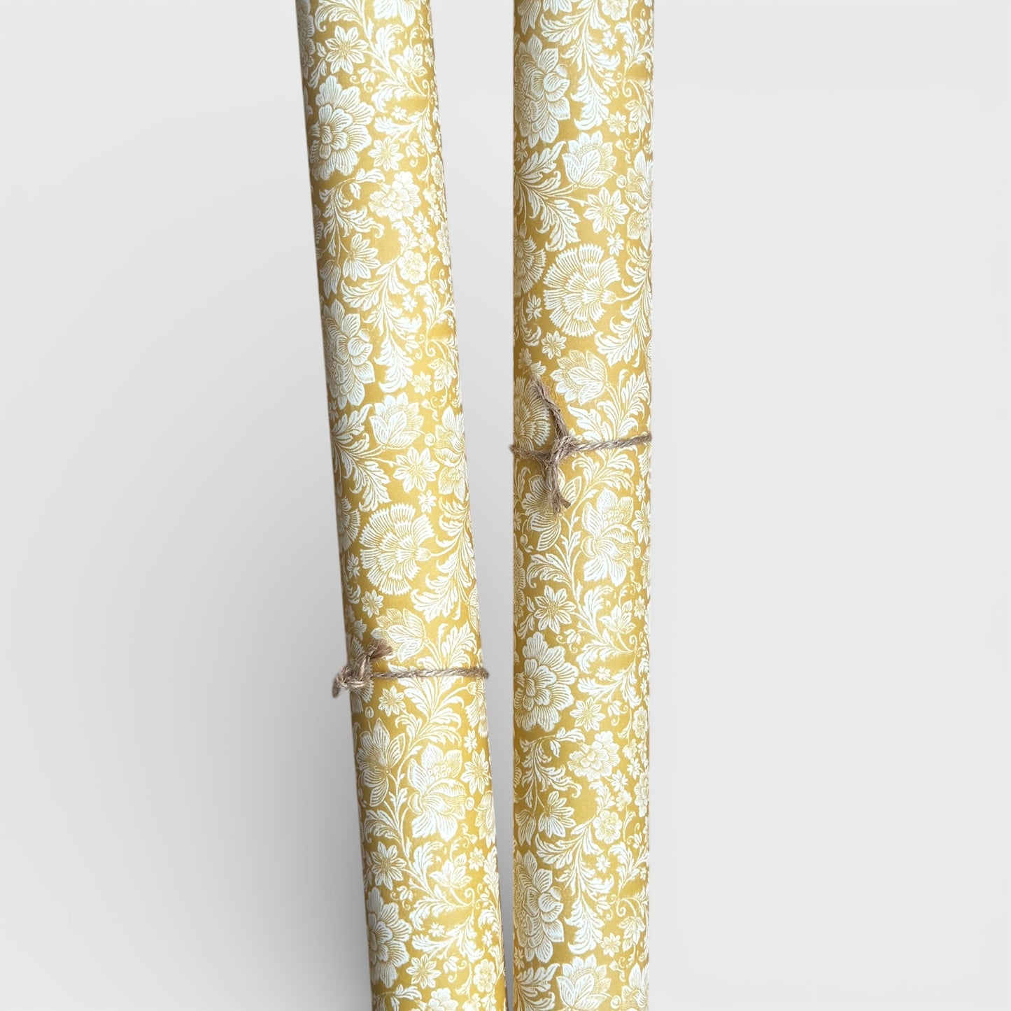 floral italian florentine wrapping paper with a white repeat floral on a mustard background. Pictured rolled