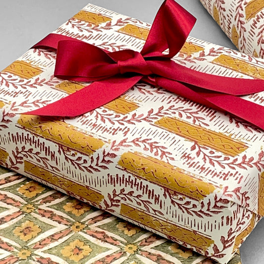 italian Remondini patterned wrapping paper by Tassotti. Mustard stripes with burgundy block printed garland on cream backdrop.  Wrapped as a present with a red ribbon bow