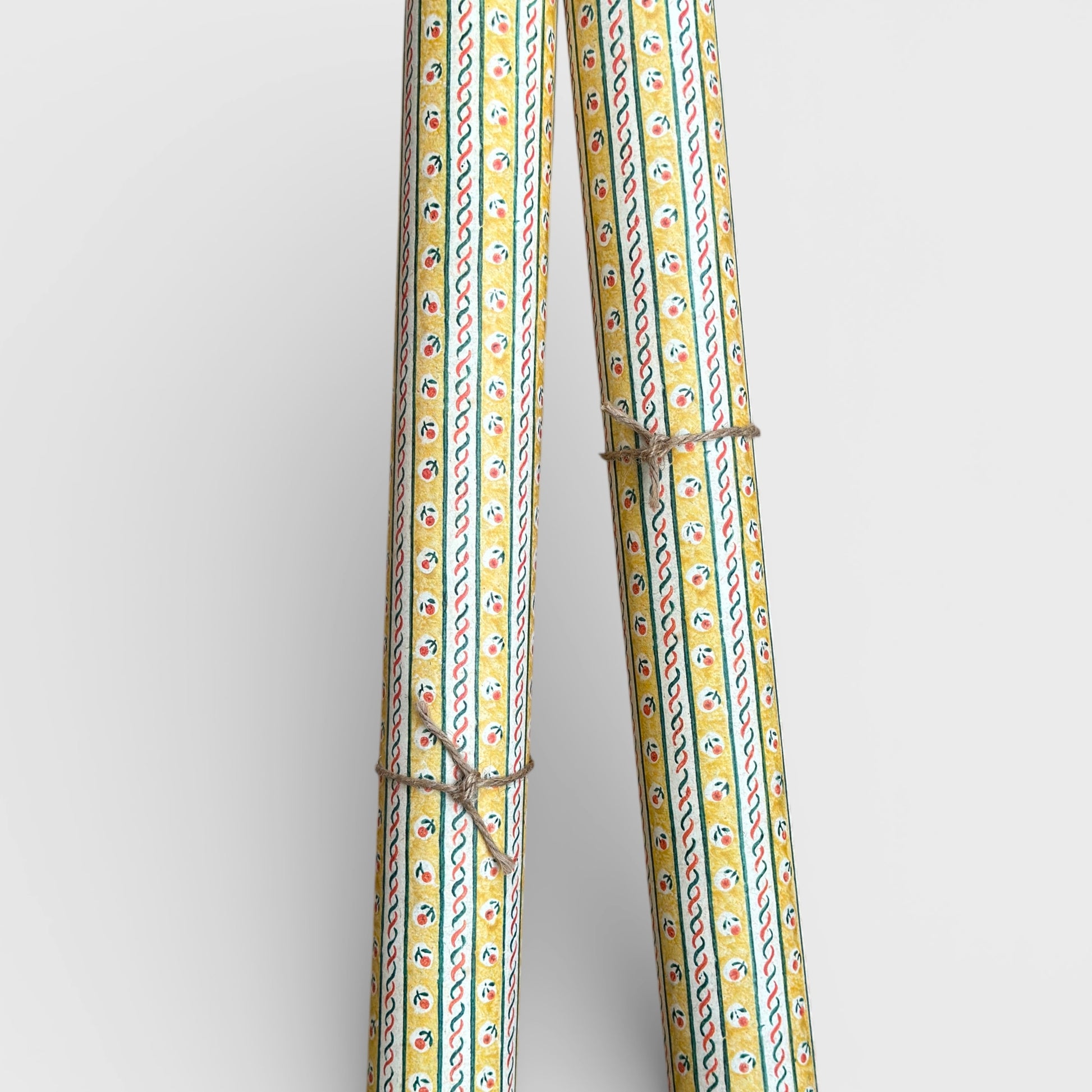 a sheet of florentine italian wrapping paper with a striped design in yellow, green, red and white with a little flower block print between the stripes. Pictured rolled