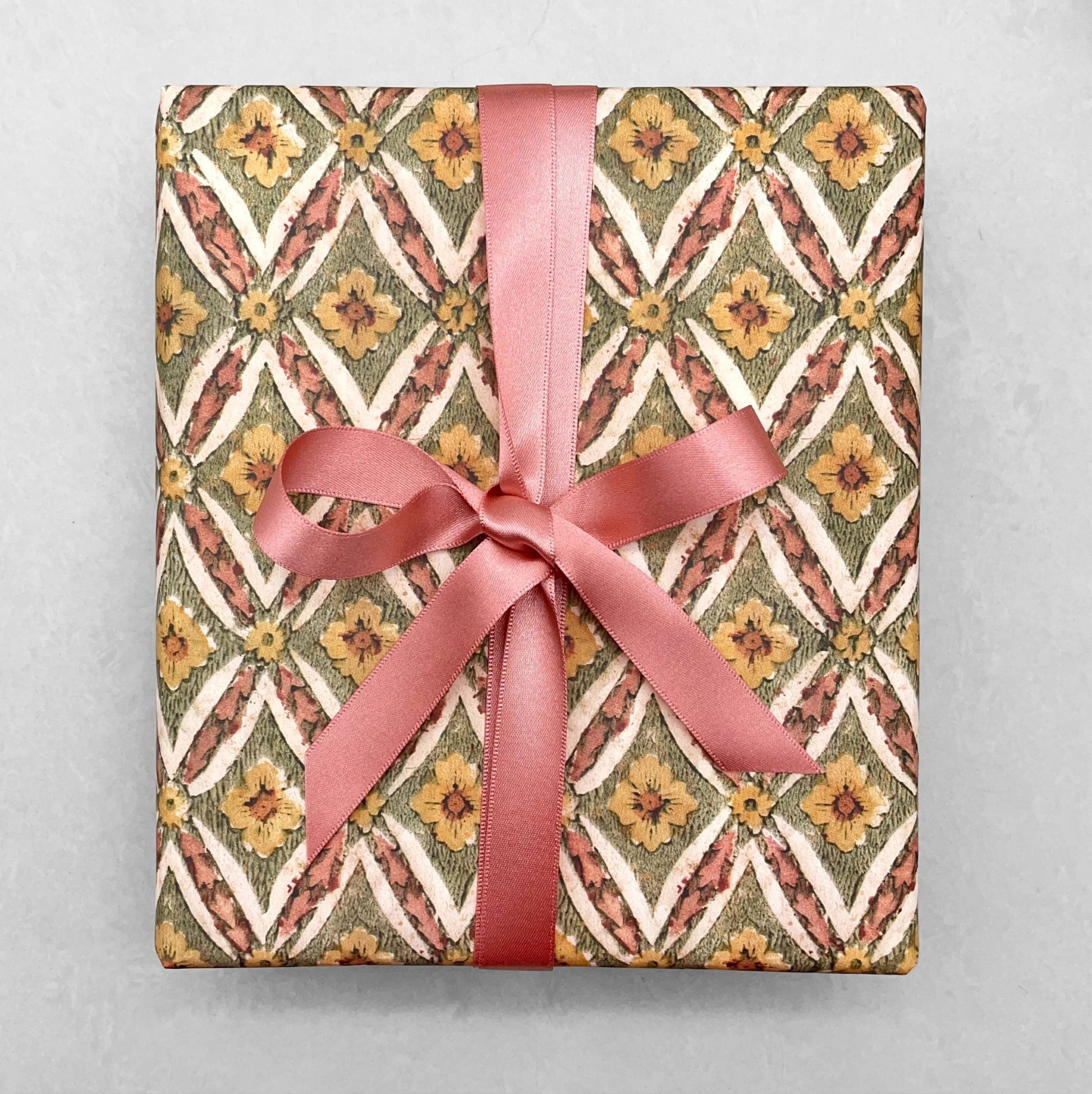 italian Remondini patterned wrapping paper by Tassotti. a repeat diamond pattern with flowers in sage green, soft peach and yellow on white background. Wrapped with a pink ribbon bow