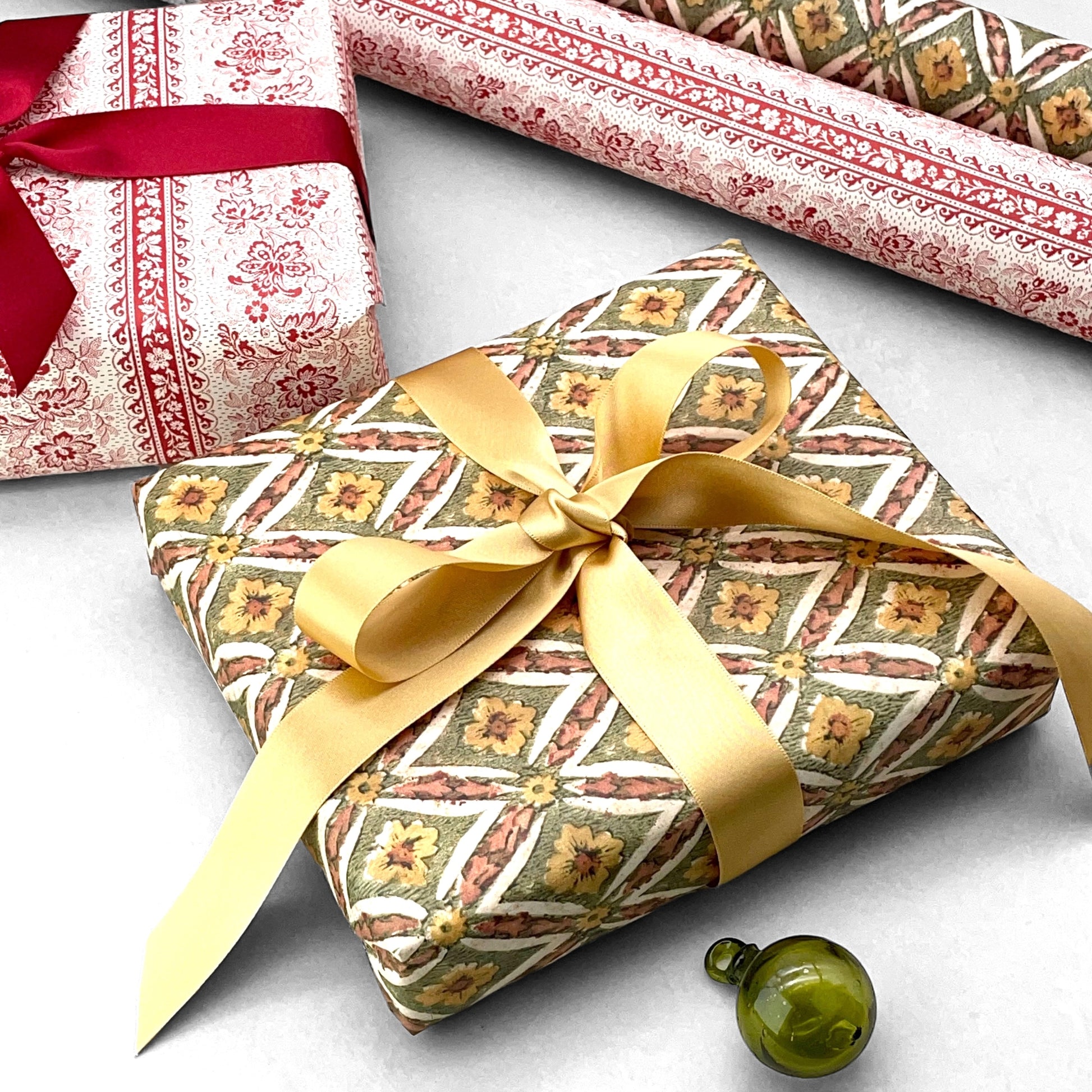 italian Remondini patterned wrapping paper by Tassotti. a repeat diamond pattern with flowers in sage green, soft peach and yellow on white background. Wrapped as a present with a gold bow
