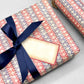 italian Remondini patterned wrapping paper by Tassotti. Striped design with bands red and blue with a cut out diamond effect in cream.  Pictured as a present with navy bow and tag