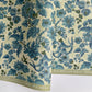 a sheet of wrapping paper by The Kensington Paperie with a large chintz floral in teal blue, with green foliage and a speckled light green ground 