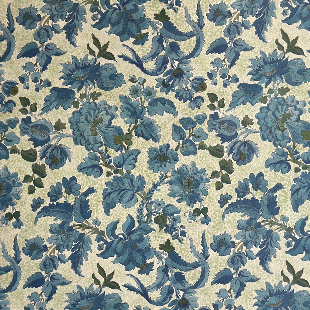 a sheet of wrapping paper by The Kensington Paperie with a large chintz floral in teal blue, with green foliage and a speckled light green ground 