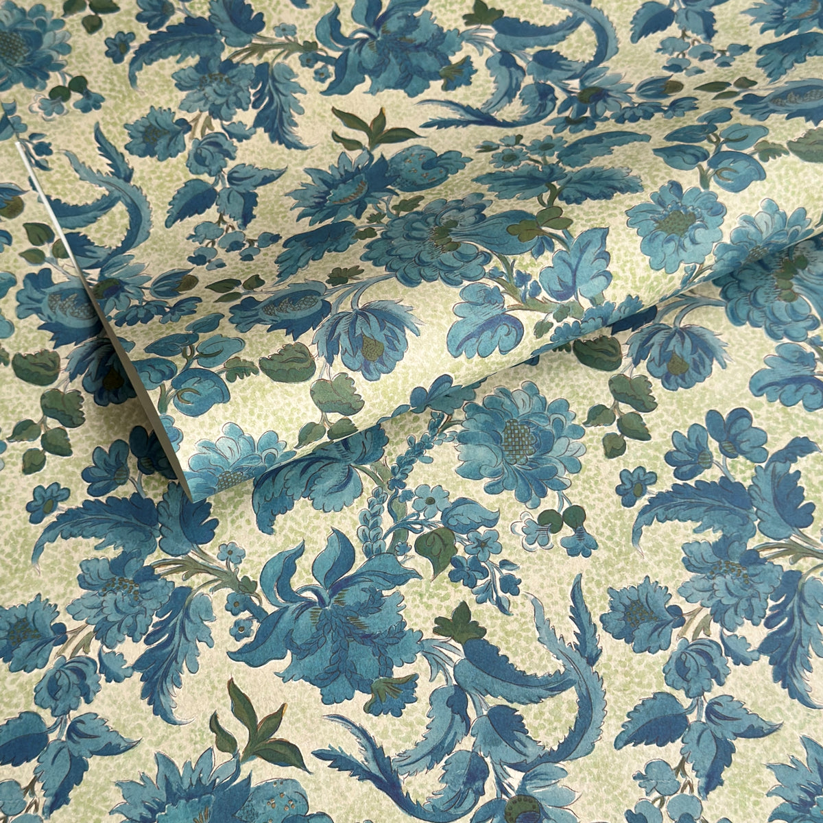 a sheet of wrapping paper by The Kensington Paperie with a large chintz floral in teal blue, with green foliage and a speckled light green ground 