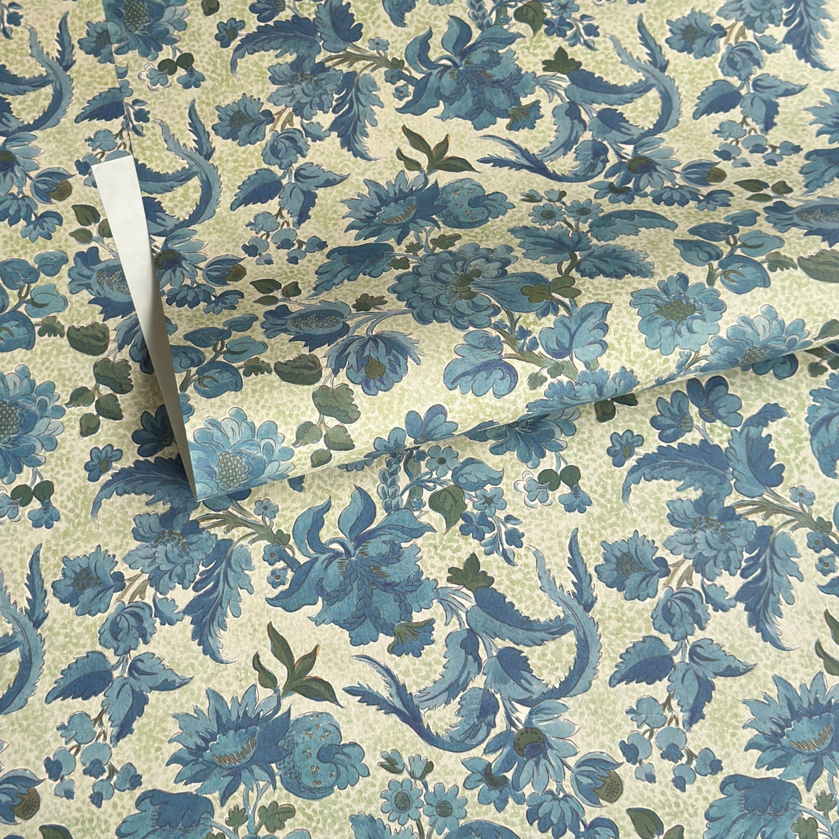 a sheet of wrapping paper by The Kensington Paperie with a large chintz floral in teal blue, with green foliage and a speckled light green ground 