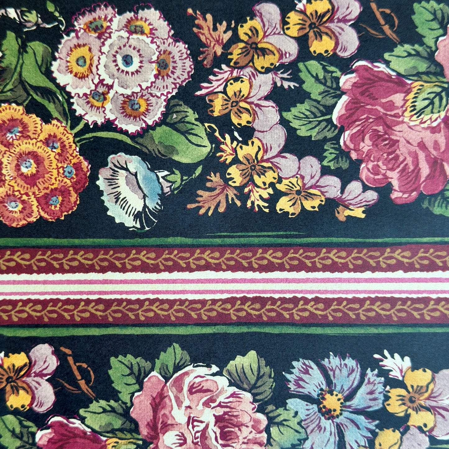 A sheet of wrapping paper, showing a detailed pattern of pink, white, and yellow flowers with green leaves on a black, bordered by horizontal stripes in pink, white, and brown.