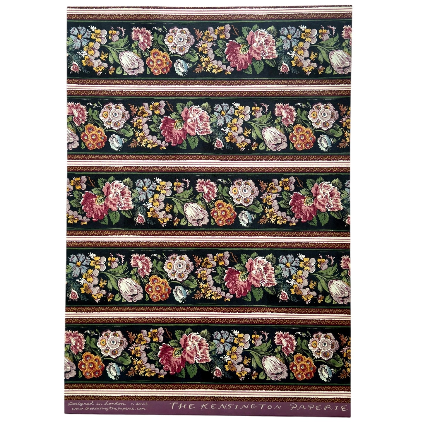 A sheet of wrapping paper, showing a detailed pattern of pink, white, and yellow flowers with green leaves on a black, bordered by horizontal stripes in pink, white, and brown.