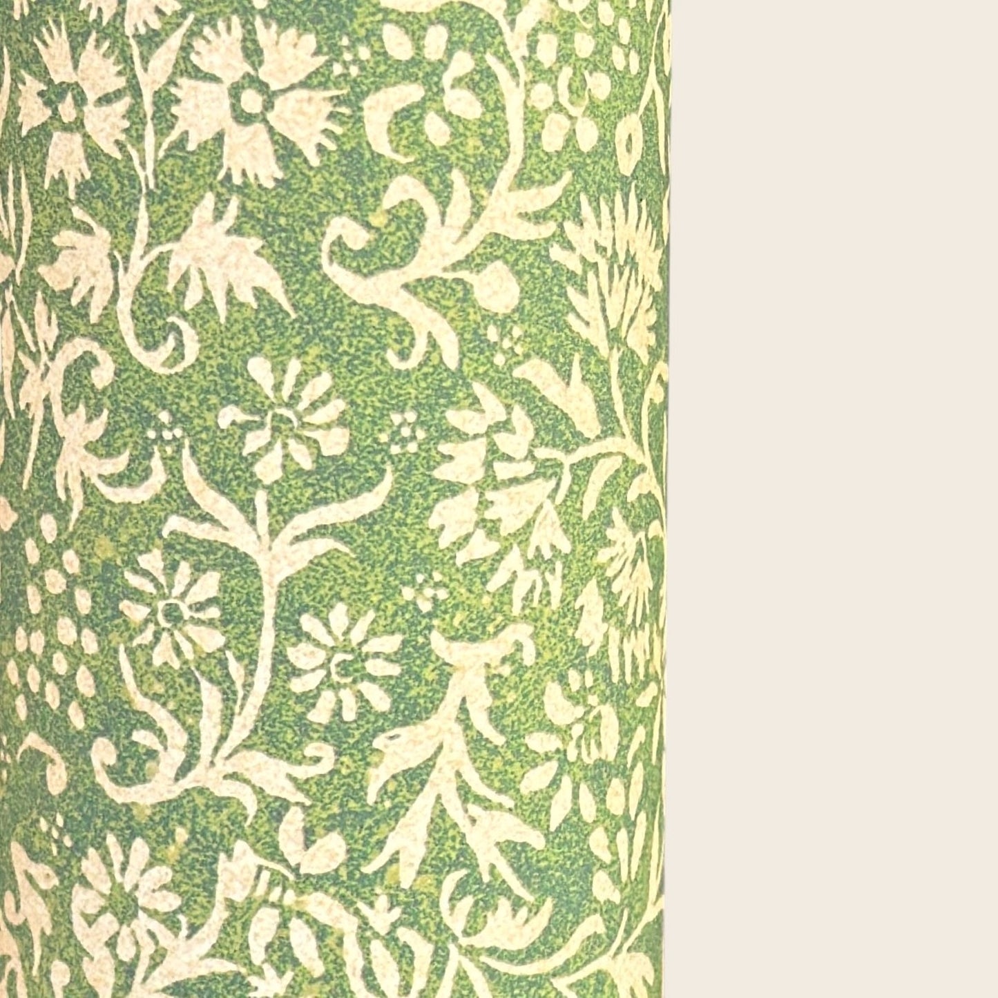 A sheet of green wrapping paper with a dense cream floral and vine pattern, shown partially unrolled on a white background. 