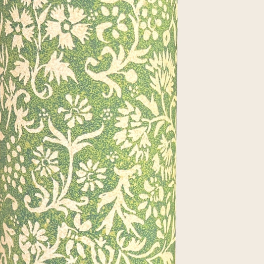 A sheet of green wrapping paper with a dense cream floral and vine pattern, shown partially unrolled on a white background. 