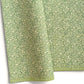 A sheet of green wrapping paper with a dense cream floral and vine pattern, shown partially unrolled on a white background. 