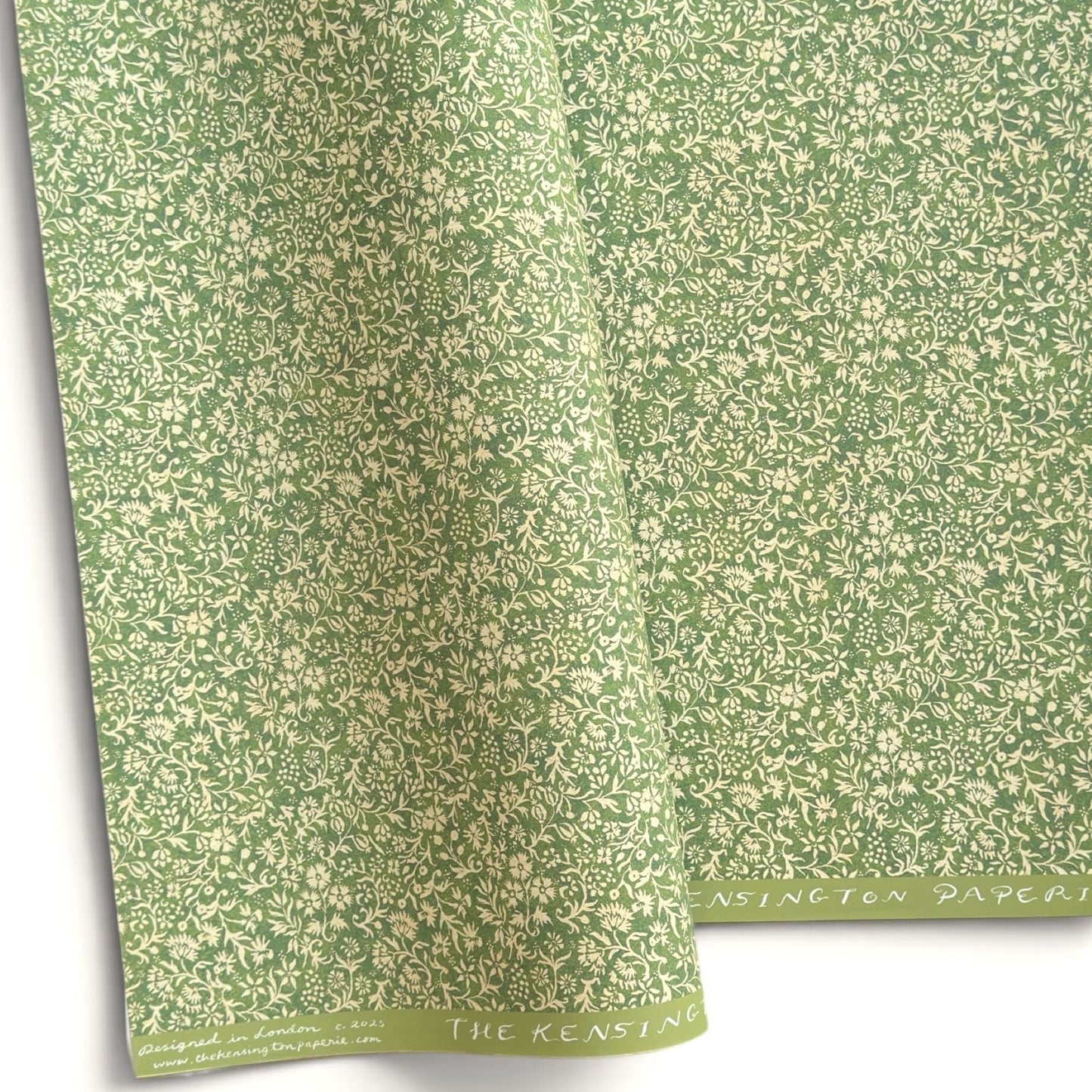 A sheet of green wrapping paper with a dense cream floral and vine pattern, shown partially unrolled on a white background. 