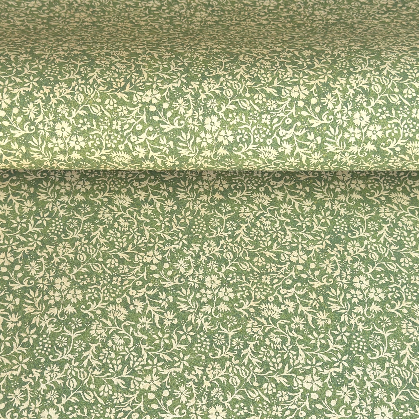 A sheet of green wrapping paper with a dense cream floral and vine pattern, shown partially unrolled on a white background. 