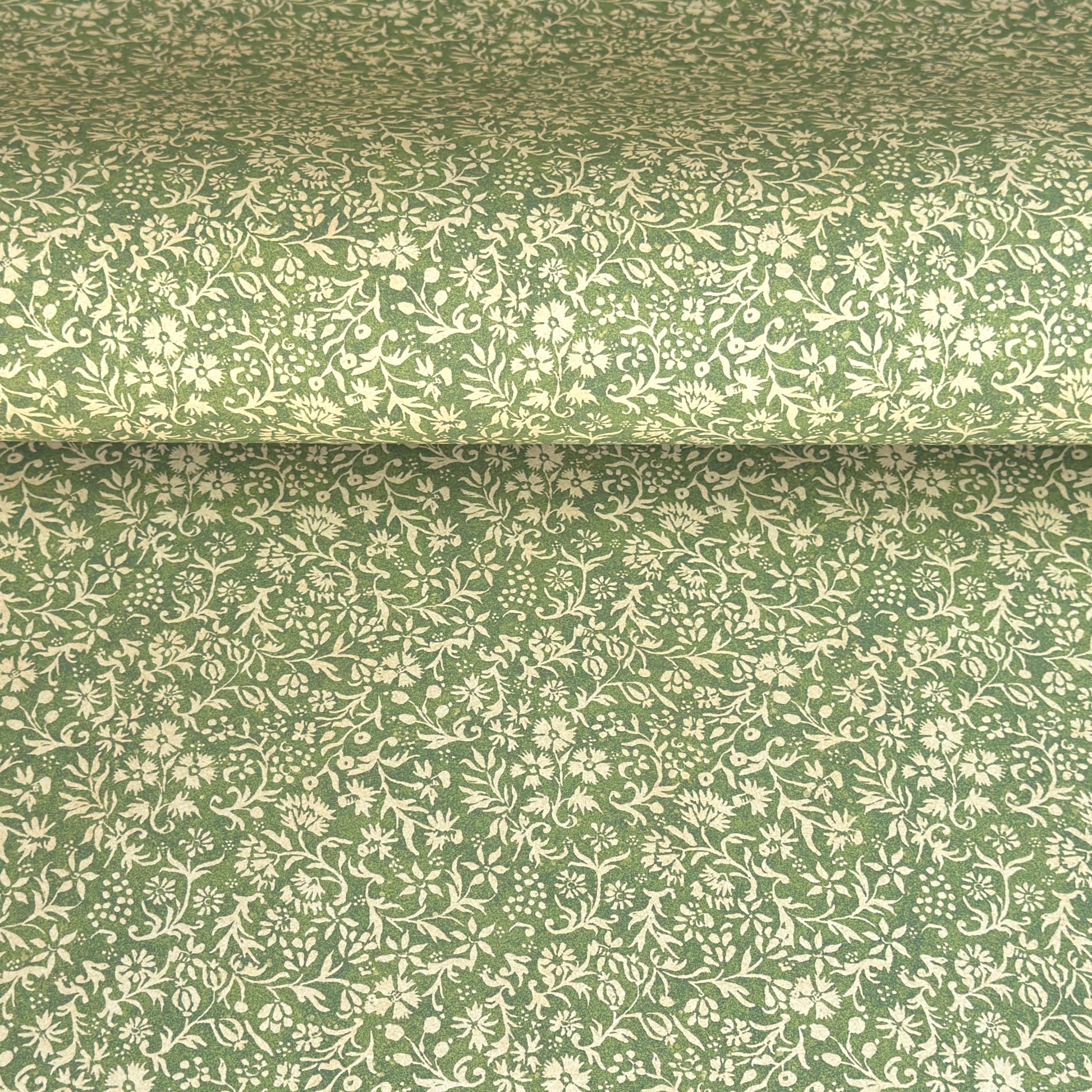 A sheet of green wrapping paper with a dense cream floral and vine pattern, shown partially unrolled on a white background. 