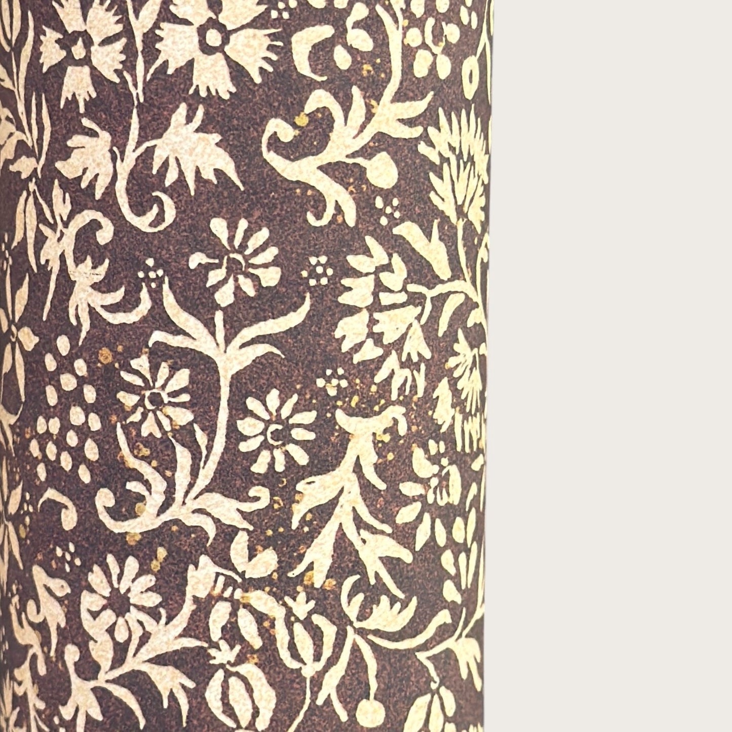 A sheet of dark aubergine wrapping paper with a dense cream floral and vine pattern