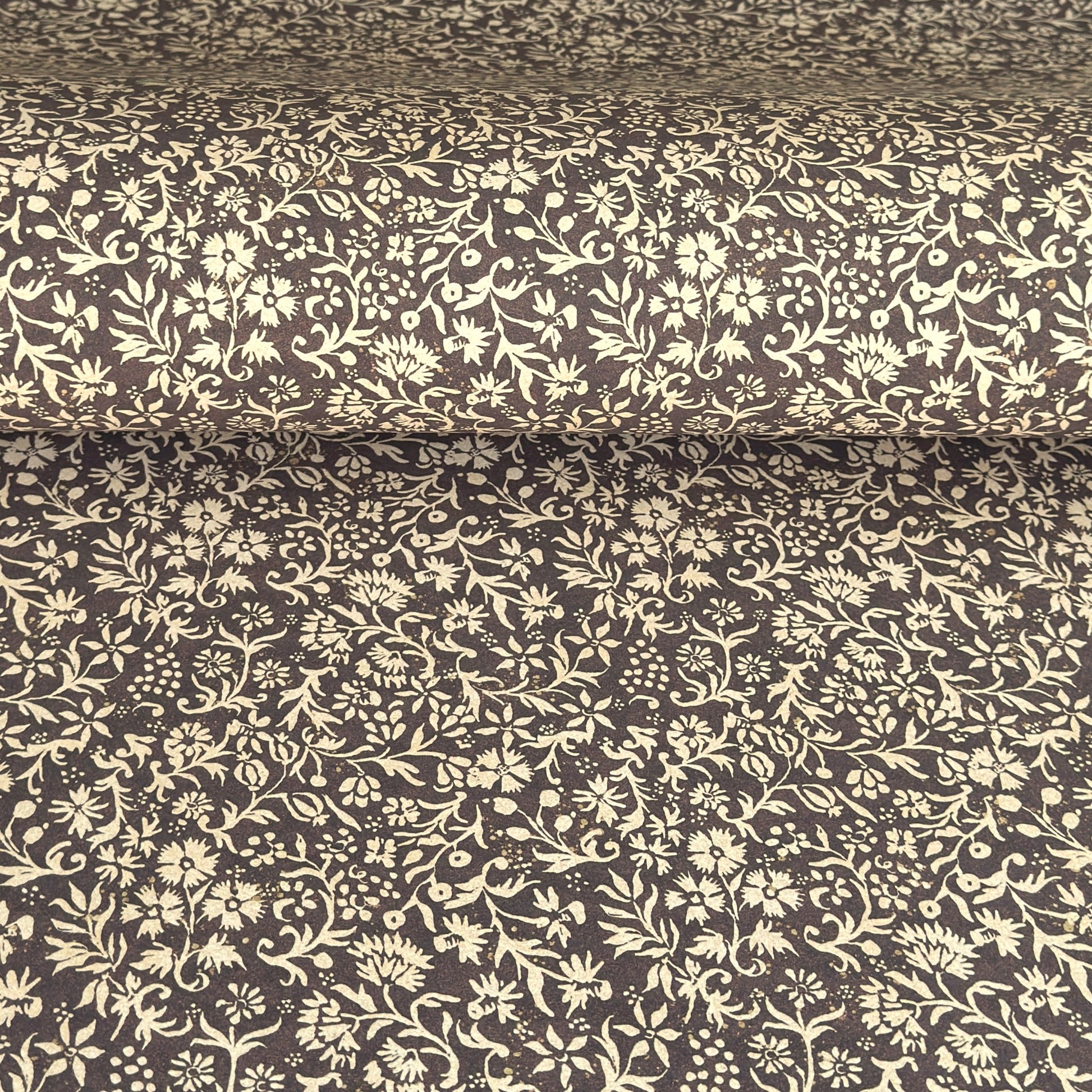 A sheet of dark aubergine wrapping paper with a dense cream floral and vine pattern