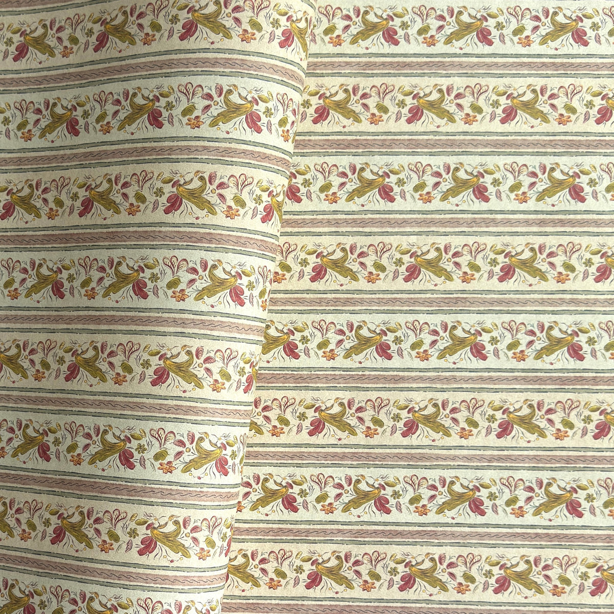 A close-up of patterned wrapping paper with horizontal stripes and a repeating floral vine motif in muted green, pink, and brown on an off-white background. 