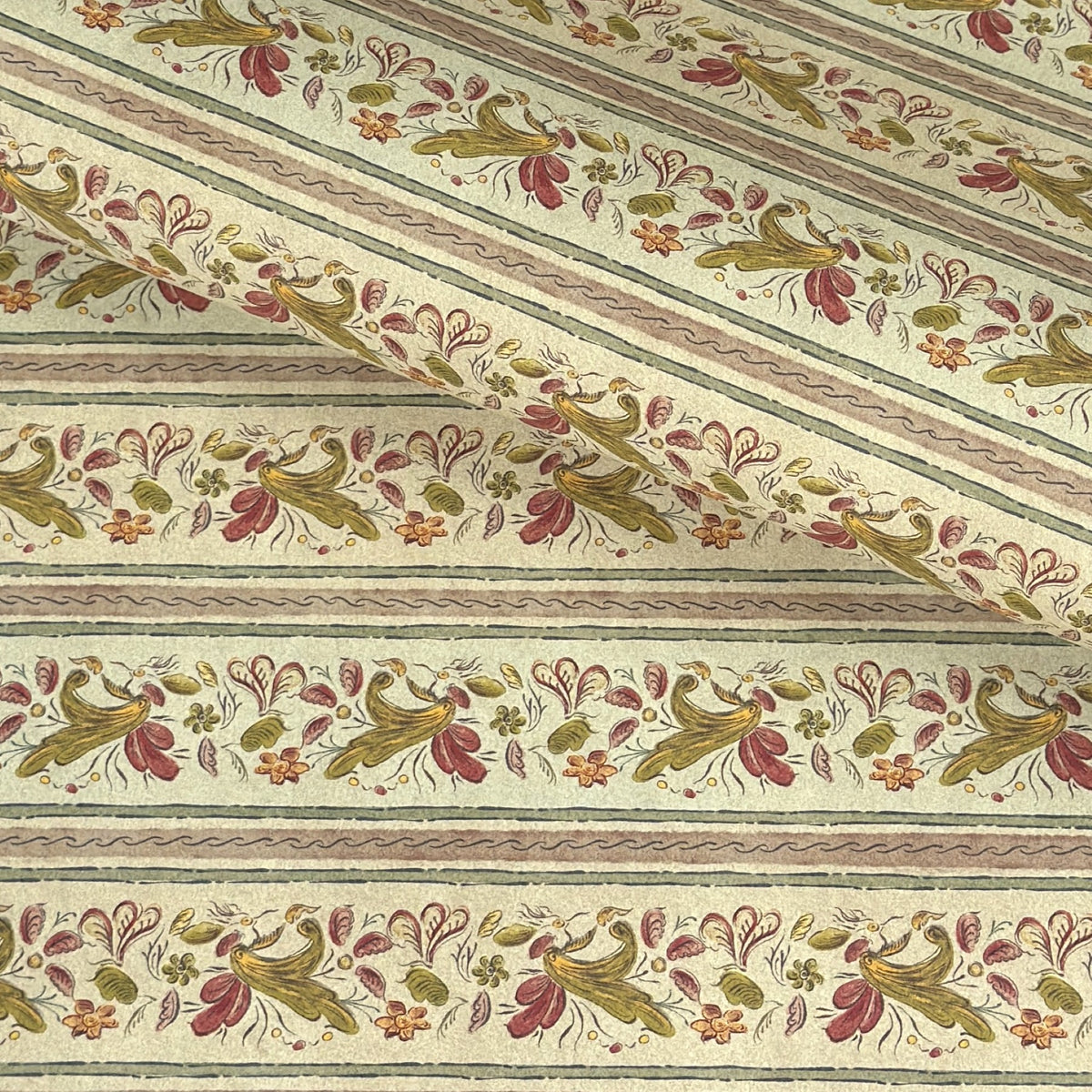 A close-up of patterned wrapping paper with horizontal stripes and a repeating floral vine motif in muted green, pink, and brown on an off-white background. 