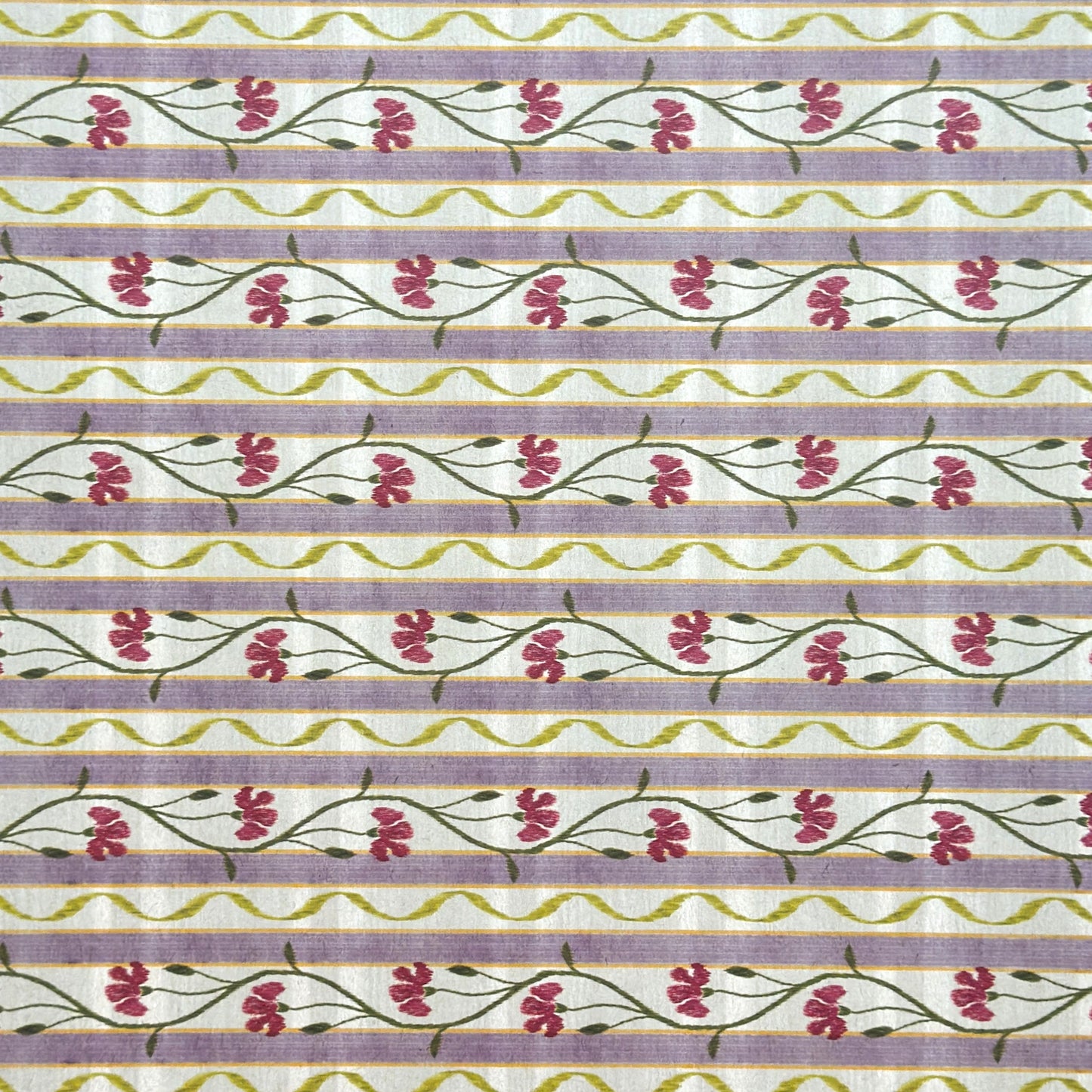 A close-up of a patterned wrapping paper featuring horizontal lavender and cream stripes with pink flowers, green stems, and olive-green wavy lines.