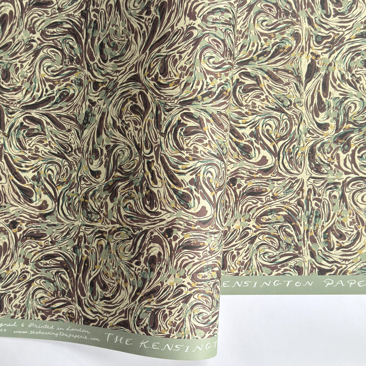 a printed marbled wrapping paper sheet with swirling brown, beige, muted green, and small yellow accents. By The Kensington Paperie brand