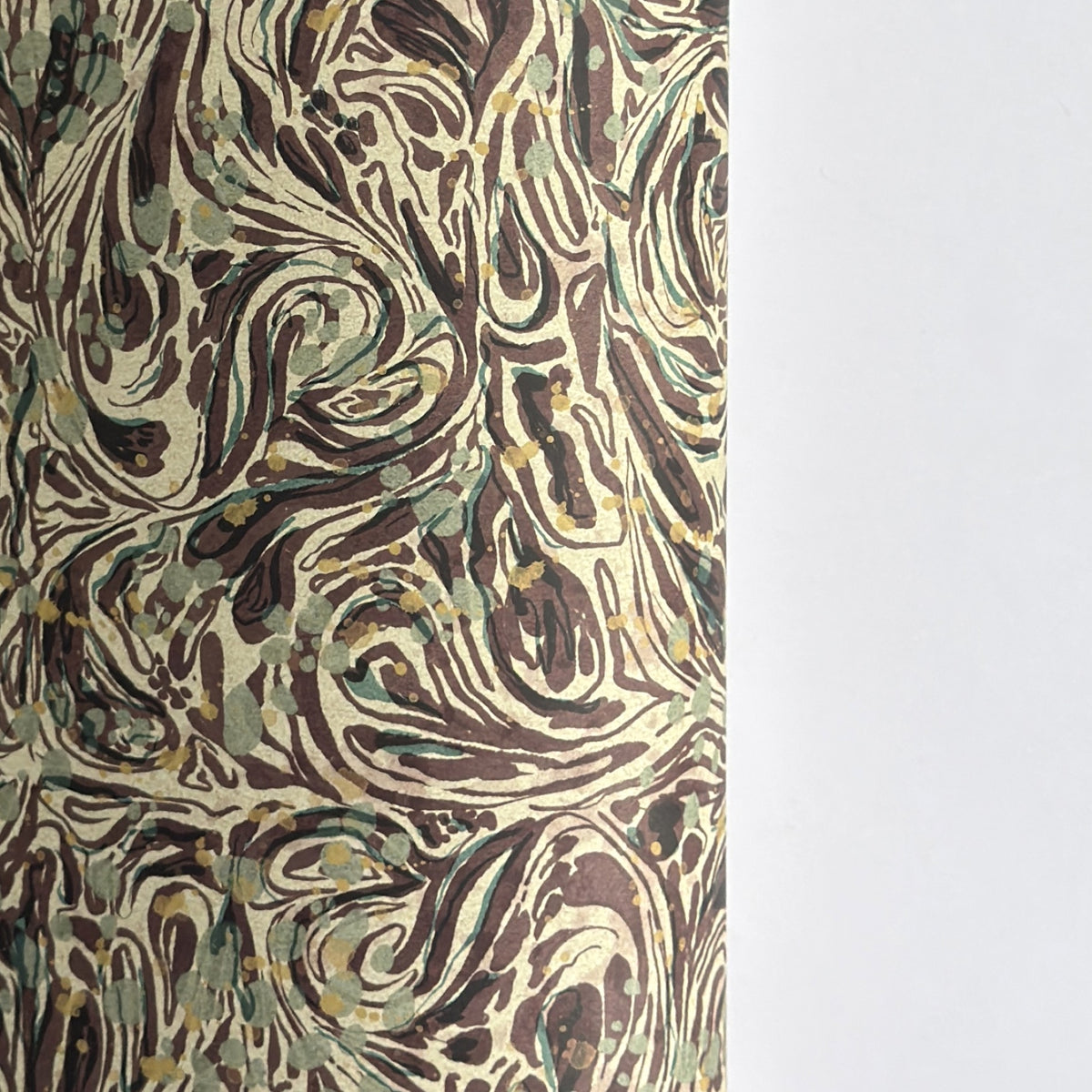 A close-up of a printed marbled wrapping paper sheet with swirling brown, beige, muted green, and small yellow accents. By The Kensington Paperie brand