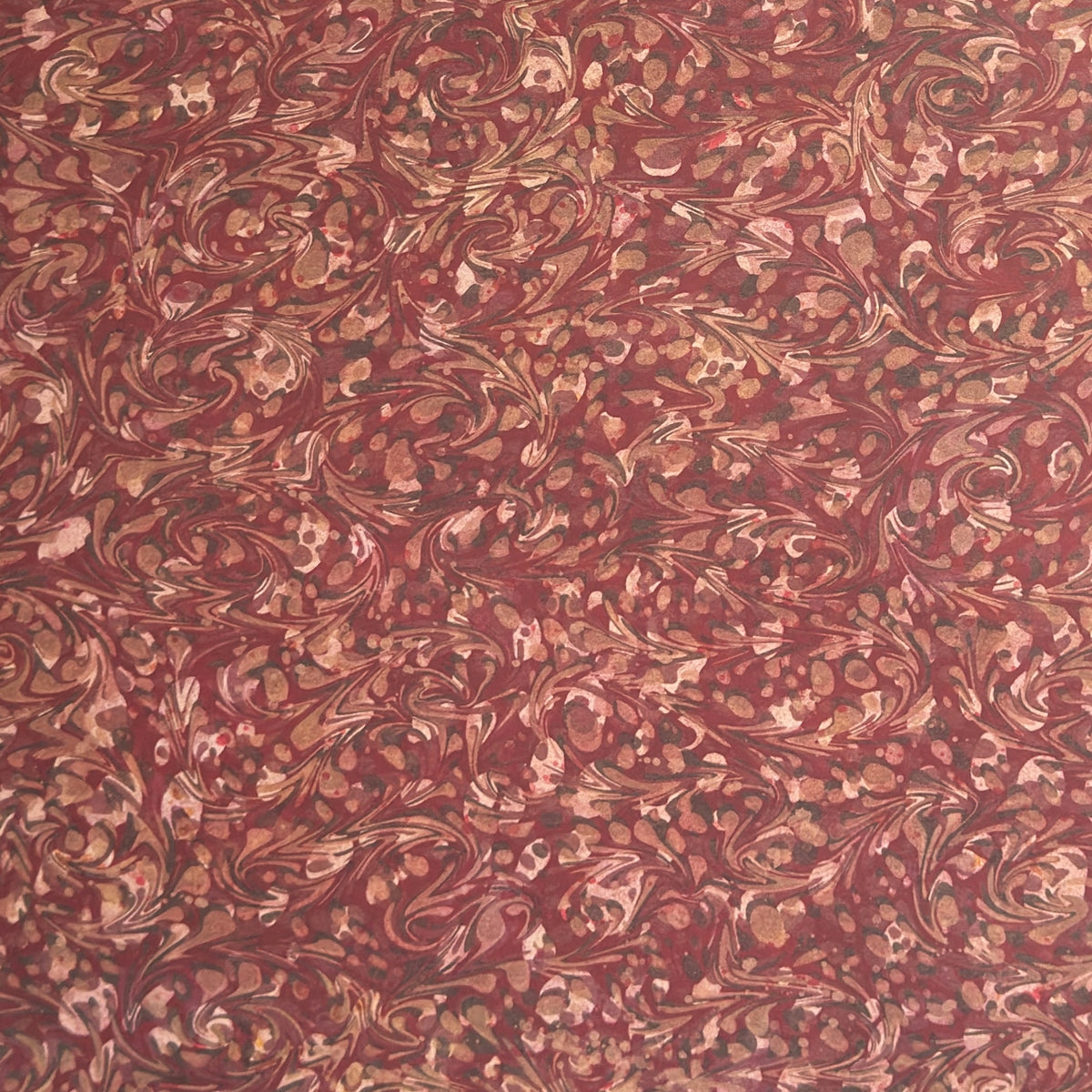 A close-up of a marbled patterned wrapping paper with swirling abstract swirls in reddish brown, rust, beige, and muted gold tones.