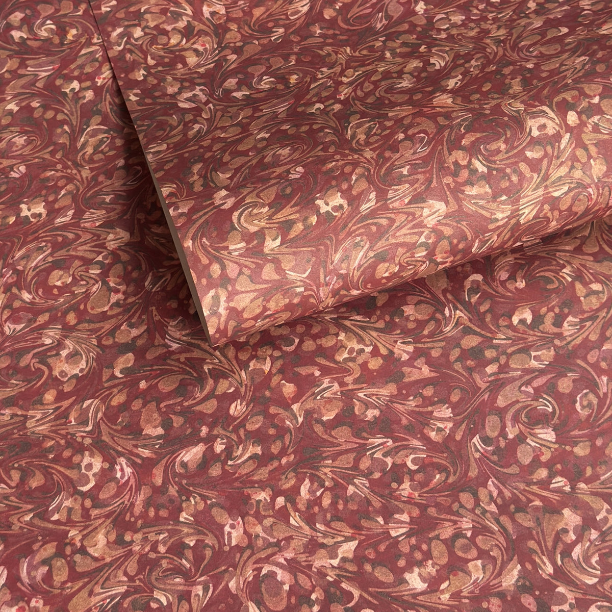 a marbled patterned wrapping paper with swirling abstract swirls in reddish brown, rust, beige, and muted gold tones.