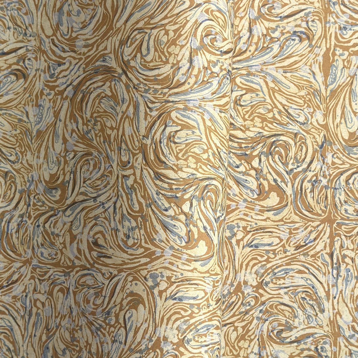 a sheet of printed marbled wrapping paper by The Kensington Paperie with a marbled swirl pattern in mustard, grey and cream