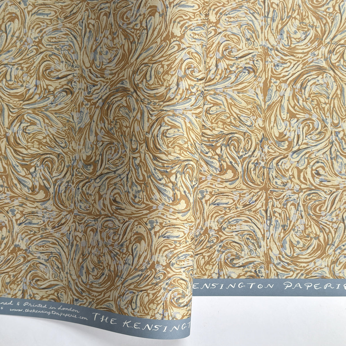 a sheet of printed marbled wrapping paper by The Kensington Paperie with a marbled swirl pattern in mustard, grey and cream
