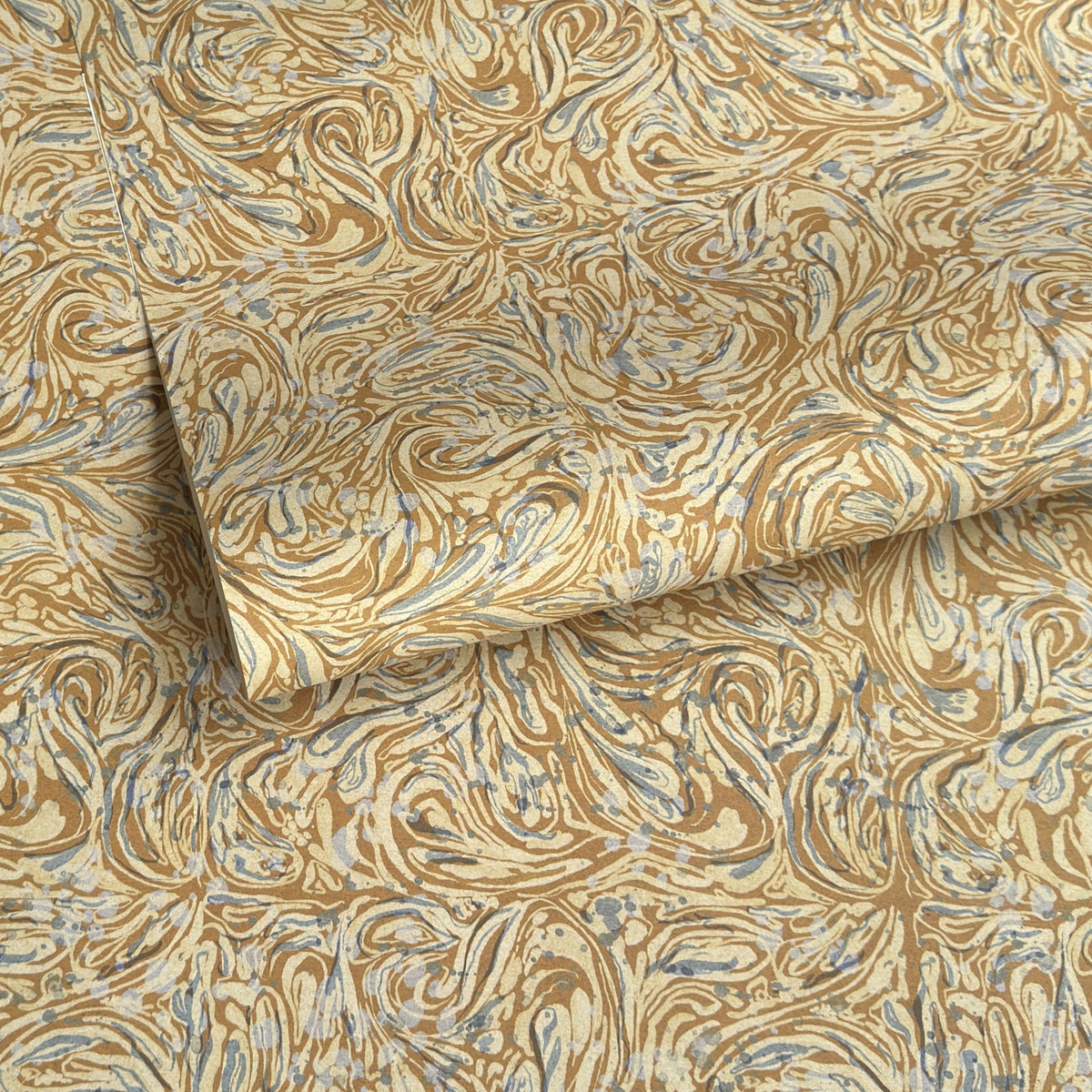 a sheet of printed marbled wrapping paper by The Kensington Paperie with a marbled swirl pattern in mustard, grey and cream