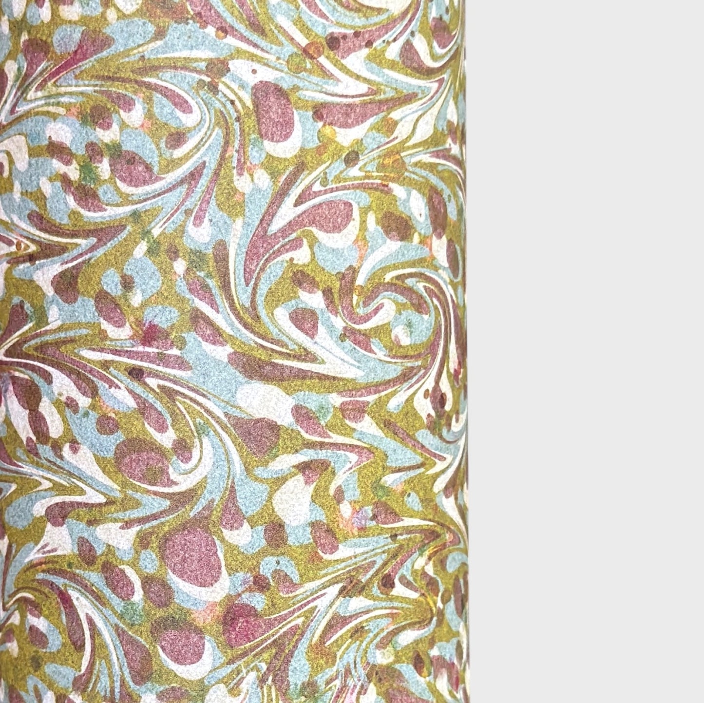 A close-up of a marbled patterned paper with swirling abstract swirls in muted gold, dusty pink, pale blue, and off-white, shown against a light gray background.