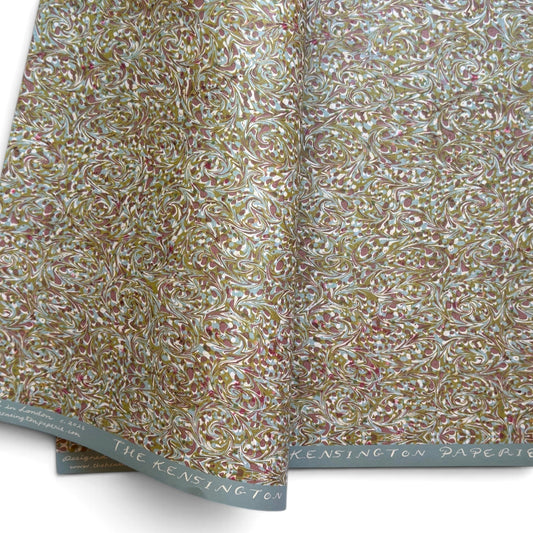 A folded roll of patterned paper with an intricate swirling floral design in muted gold, dusty rose, olive green, and white. The paper is shown folded to display both the patterned surface and the branded paper edge, which reads 'THE KENSINGTON PAPERIE'.