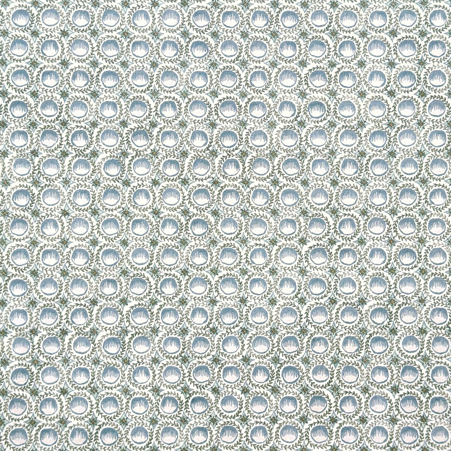 a patterned wrapping paper featuring a repeating botanical design with blue block printed steam puddings, green leafy wreaths, and small yellow accents on a white background.