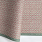 a sheet of wrapping paper by The Kensington Paperie with a small block printed geometric print in white and soft green on a cranberry ground