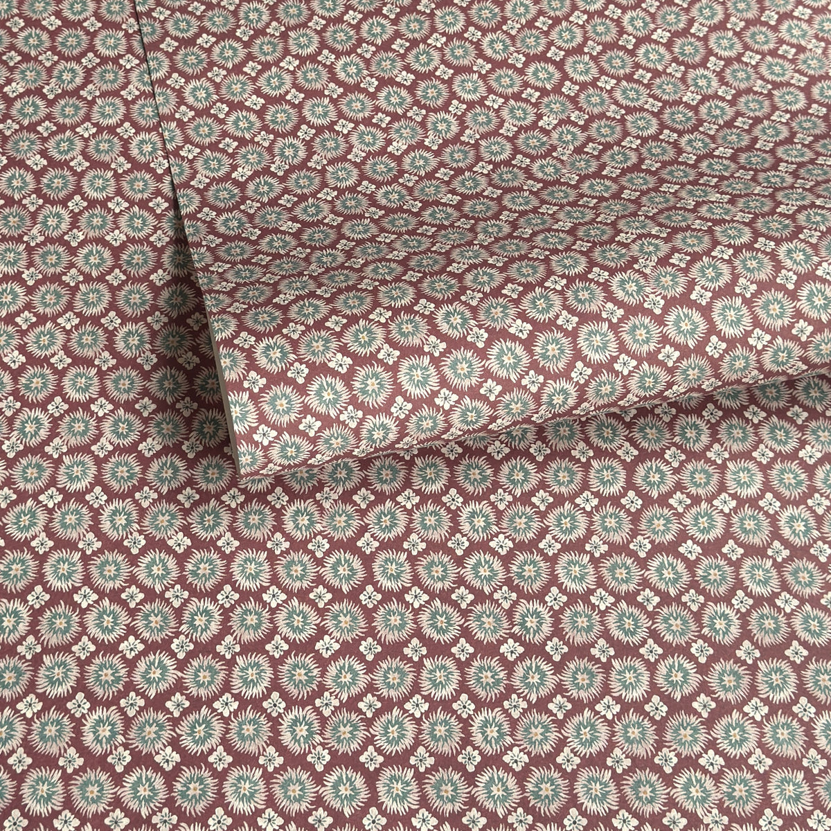 a sheet of wrapping paper by The Kensington Paperie with a small block printed geometric print in white and soft green on a cranberry ground