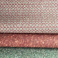 a sheet of wrapping paper by The Kensington Paperie with a small block printed geometric print in white and soft green on a cranberry ground.  Pictured rolled with a coordinating marble papers