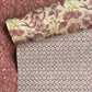 a sheet of wrapping paper by The Kensington Paperie with a small block printed geometric print in white and soft green on a cranberry ground. Pictured lightly folded with a complementary bold floral paper and a marbled design.