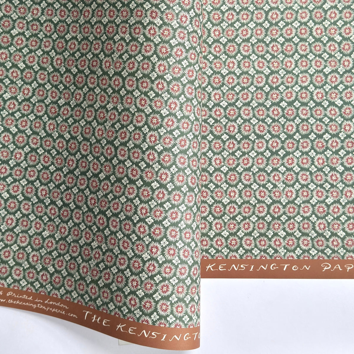 A sheet patterned wrapping paper with a repeating floral medallion design in muted green, dusty pink, and cream by The Kensington Paperie brand