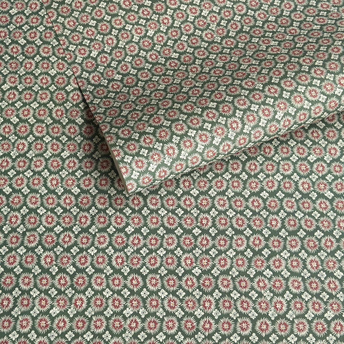 A sheet patterned wrapping paper with a repeating floral medallion design in muted green, dusty pink, and cream by The Kensington Paperie brand