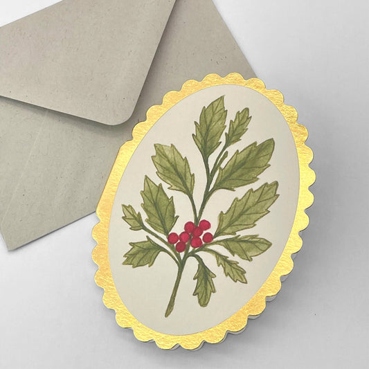 small oval card with a drawing of a sprig of holly on a cream background. the card has a gold foiled scalloped edge. By Wanderlust. With envelope