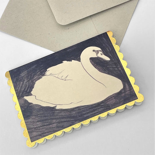 small rectangular greetings card with an image of a white swan on a black background. the card has a gold foil scalloped edge. By Wanderlust. With envelope