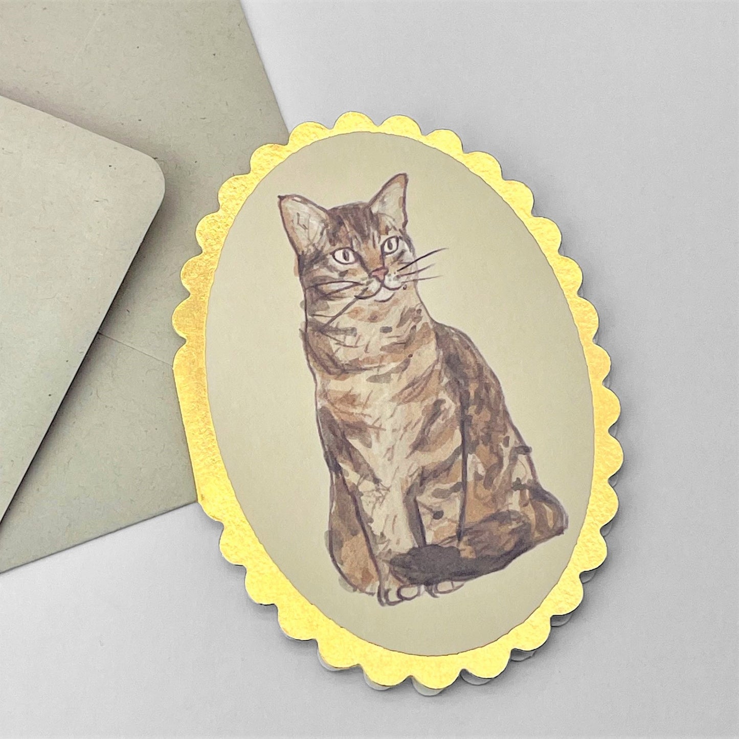 small oval greetings card with a drawing of a tabby cat. the card has a gold foiled scalloped edge. By Wanderlust. With envelope