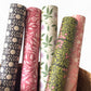 floral patterned wrapping paper in brown and cream. Pictured rolled alongside other designs