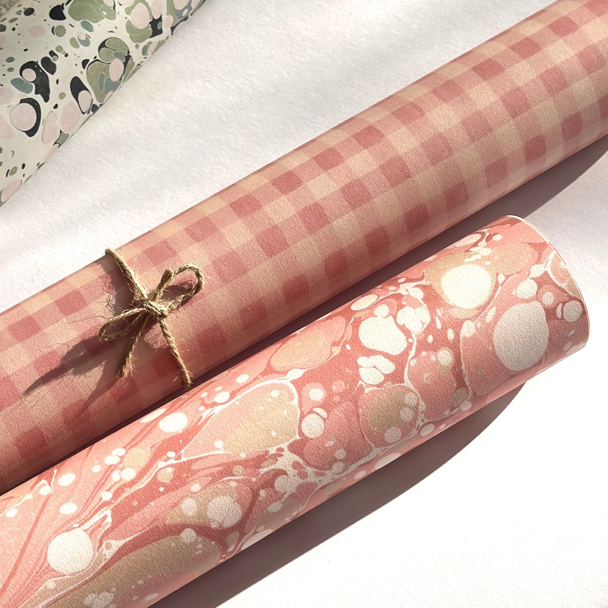 Checkered pattern wrapping paper with pink and beige squares. Pictured rolled alongside a roll of pink marbled paper