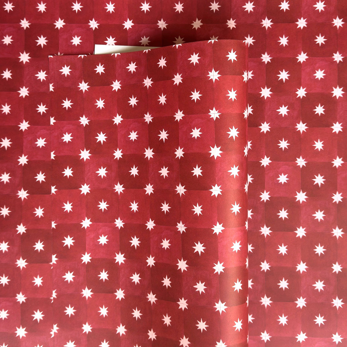 Red wrapping paper by Wanderlust with a white star pattern, shown folded to display its texture and design.