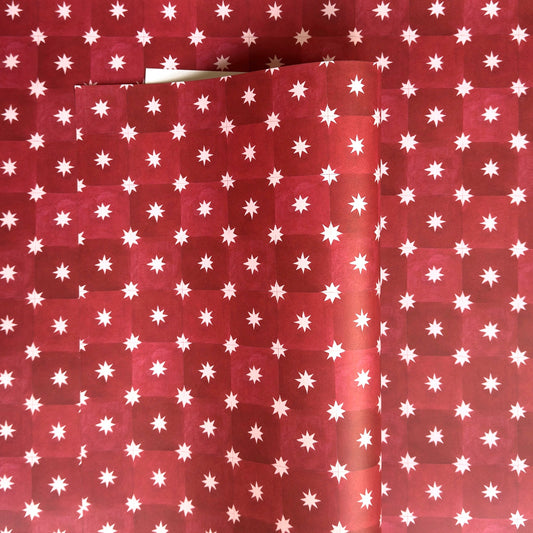 Red wrapping paper by Wanderlust with a white star pattern, shown folded to display its texture and design.