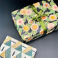 wrapping paper with green, pink, yellow and orange abstract floral repeat on black ground by Artisan Design. Design by Silver Studio