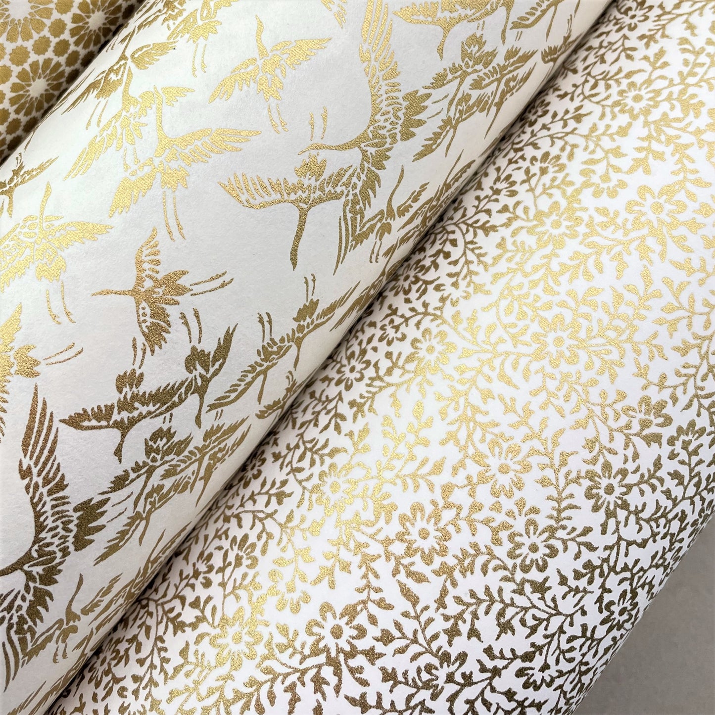 japanese silk-screen handmade paper showing a dainty gold botanical repeat design on ivory backdrop, lifestyle shot with other gold papers
